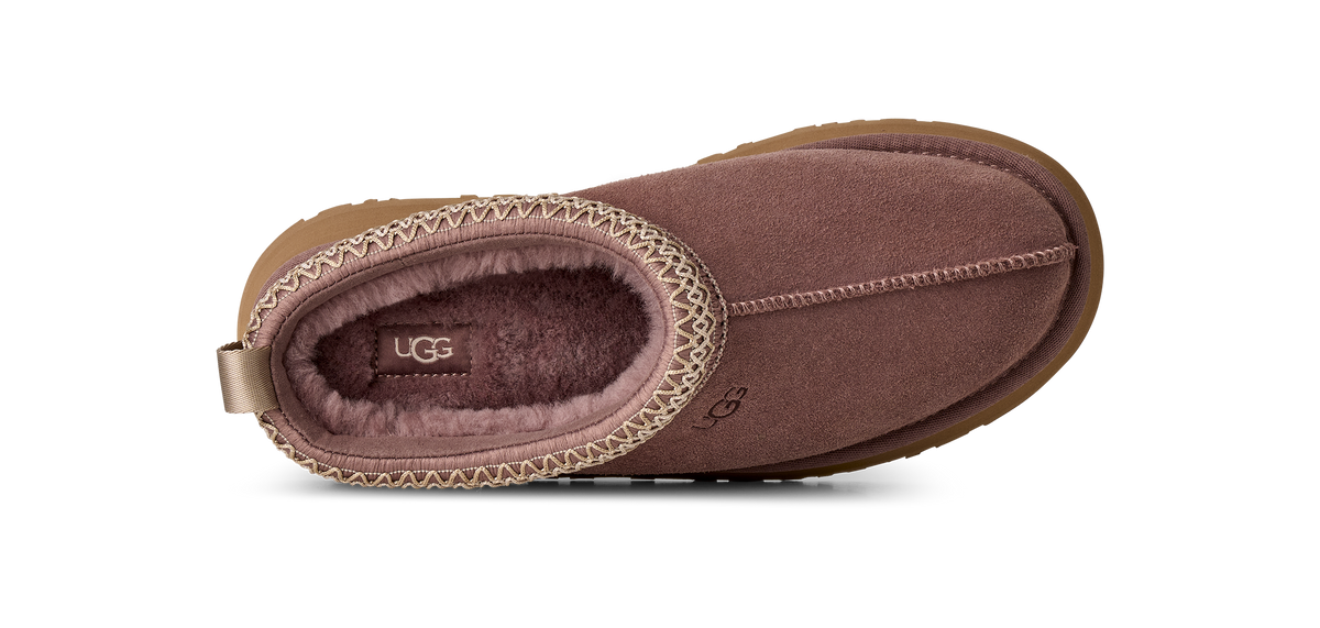 A single UGG slipper shown from a top-down view on a clean white background. The slipper features a dusty rose-brown suede exterior, a matching fuzzy interior, and a decorative stitched trim around the opening.