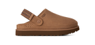 A single UGG slip-on clog shoe in a warm tan-brown suede-like material, shown from the side against a solid white background. The shoe features a patterned brown strap with a metal buckle and a thick brown sole.