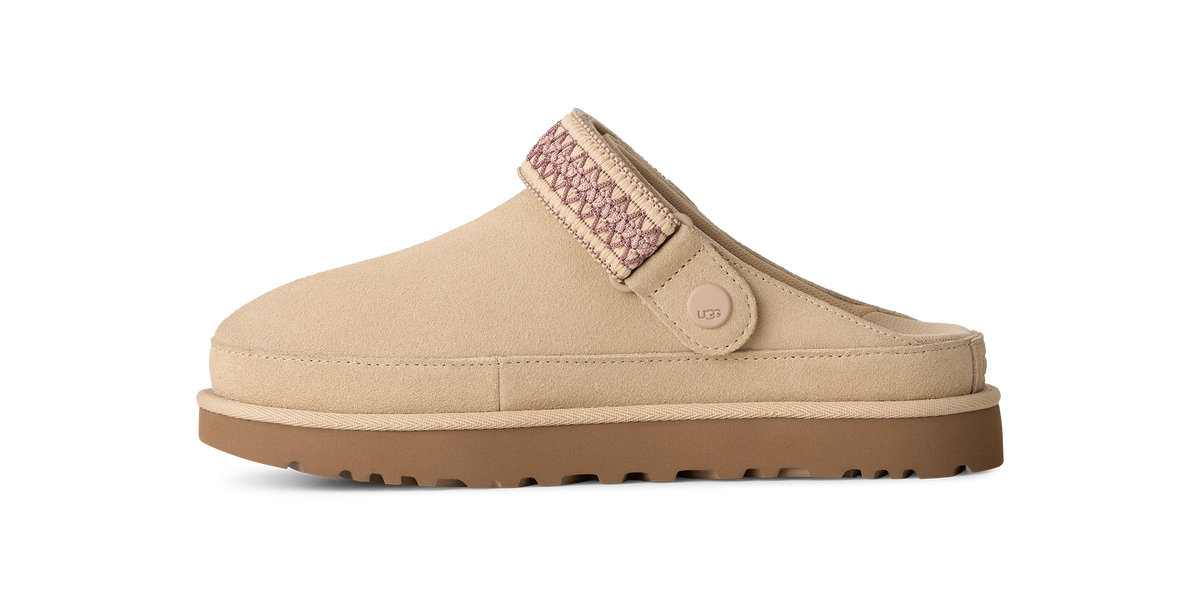 A beige slip-on clog-style shoe with a brown sole and a pink patterned strap detail, shown in profile against a white background.
