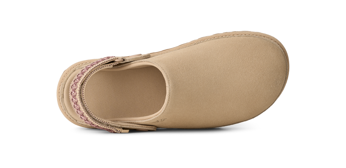 A single tan slip-on shoe shown from a top-down view on a white background, featuring a woven pink and white patterned strap around the back.