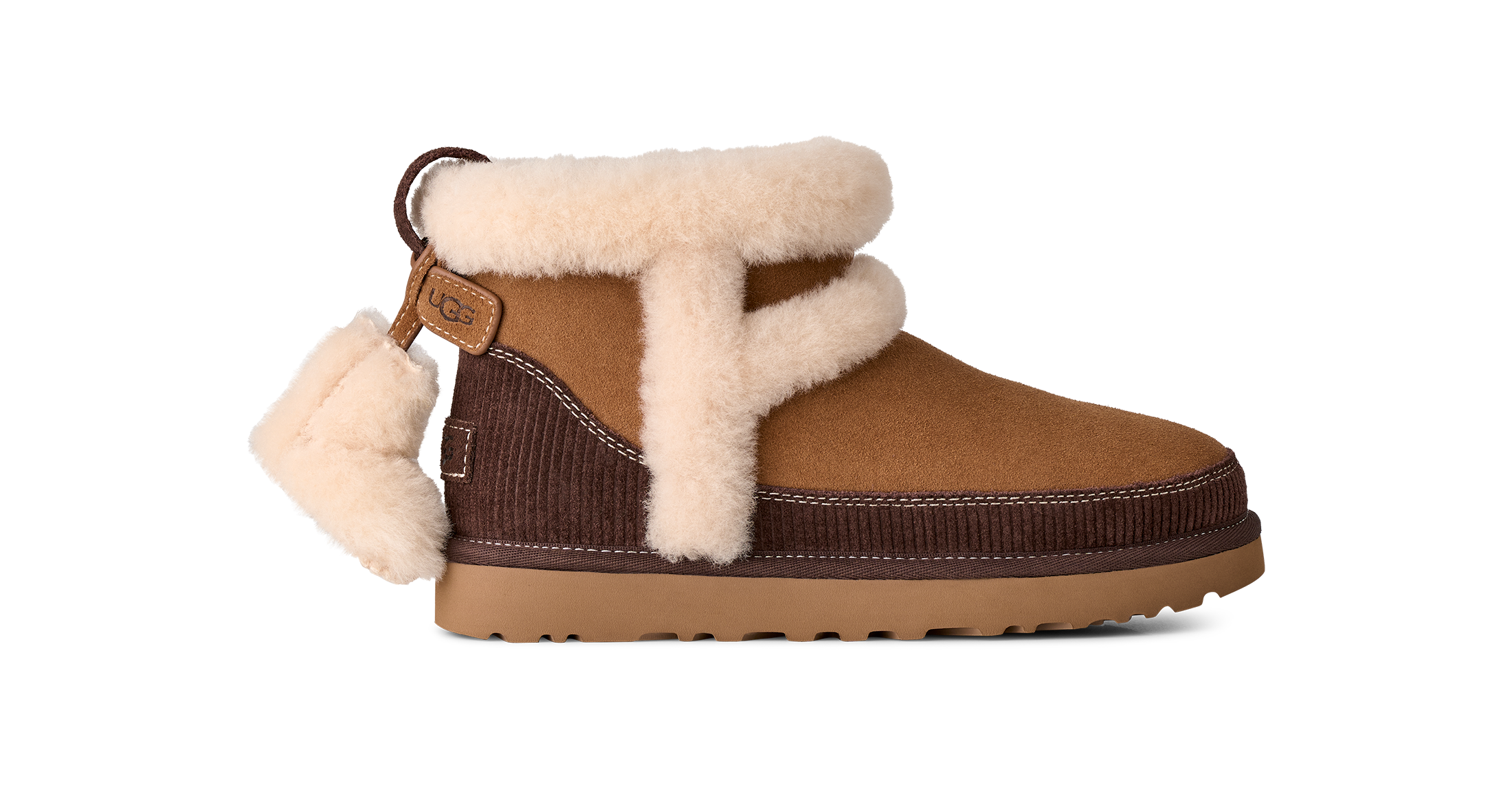 A brown suede and corduroy ankle boot with thick cream shearling lining, a decorative hanging shearling pom-pom, and a brown sole, shown against a plain white background.