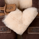 Close-up of UGG slipper boots showing the brown corduroy exterior, tan leather trim, and soft cream shearling lining.