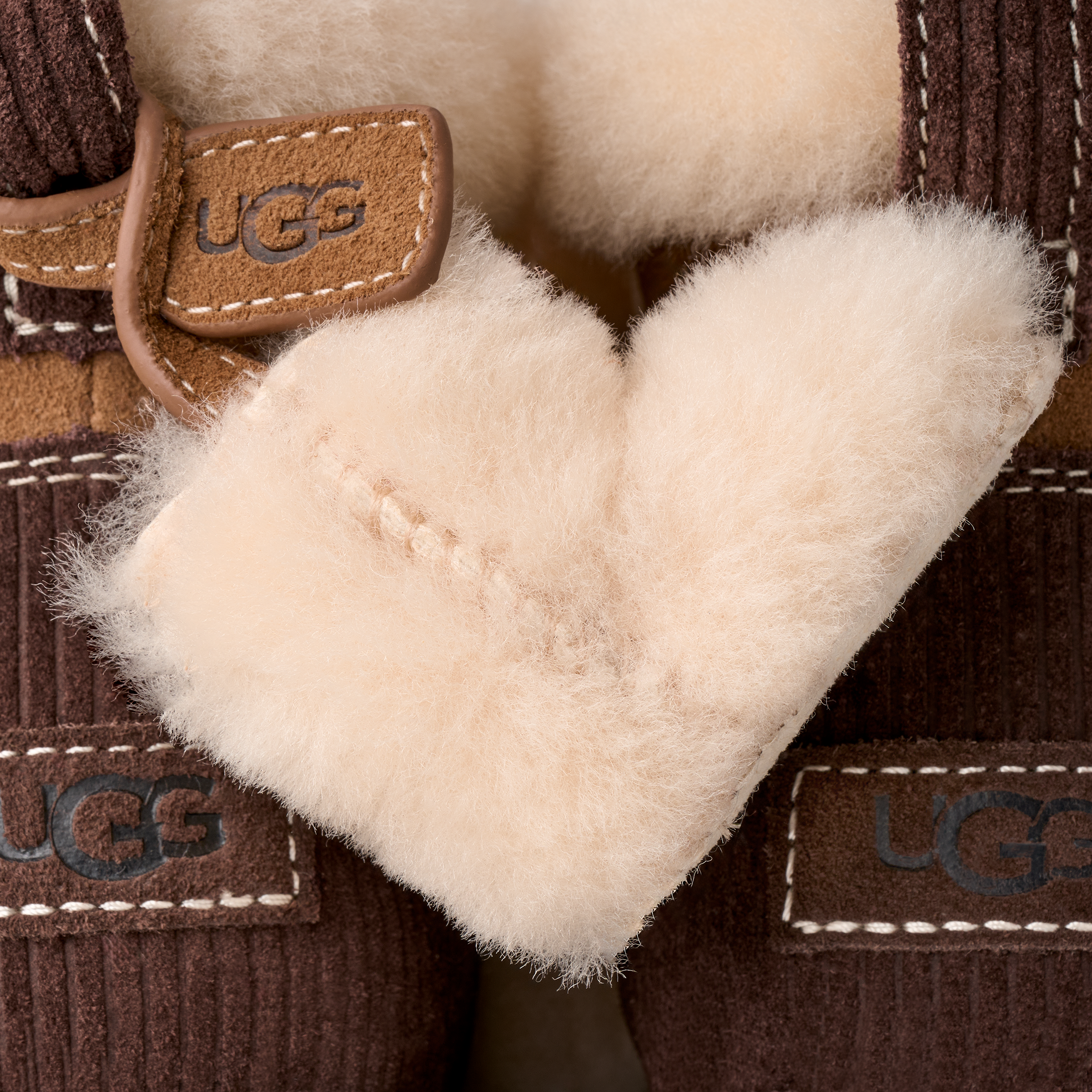 Close-up of UGG slipper boots showing the brown corduroy exterior, tan leather trim, and soft cream shearling lining.