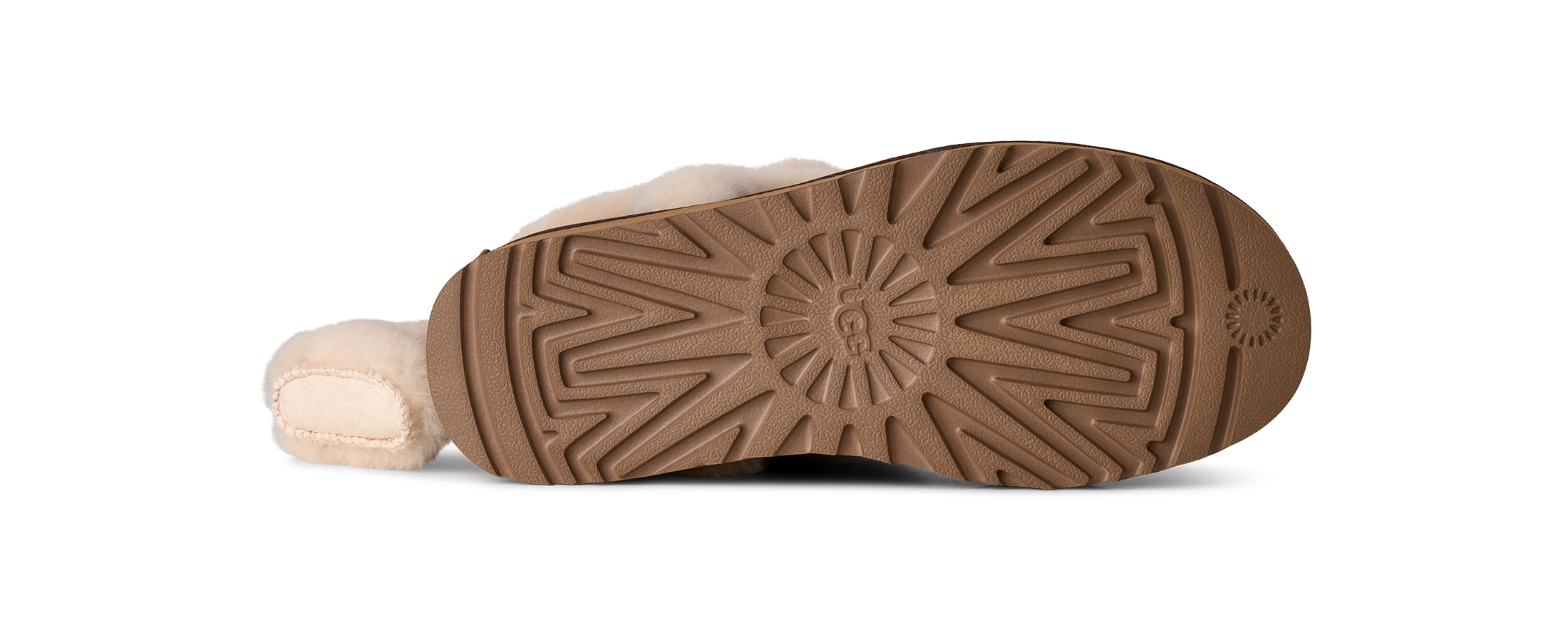 The bottom sole of a shearling boot, showing a brown treaded rubber outsole with a UGG logo embossed in the center, photographed on a white background.