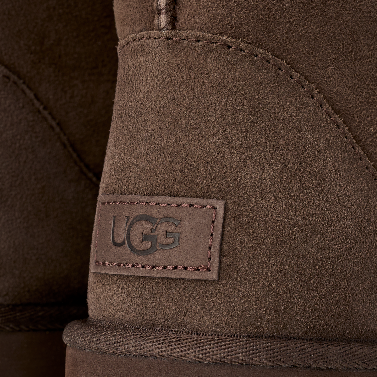 Close-up of a brown suede UGG boot showing the stitched UGG logo patch on the side.