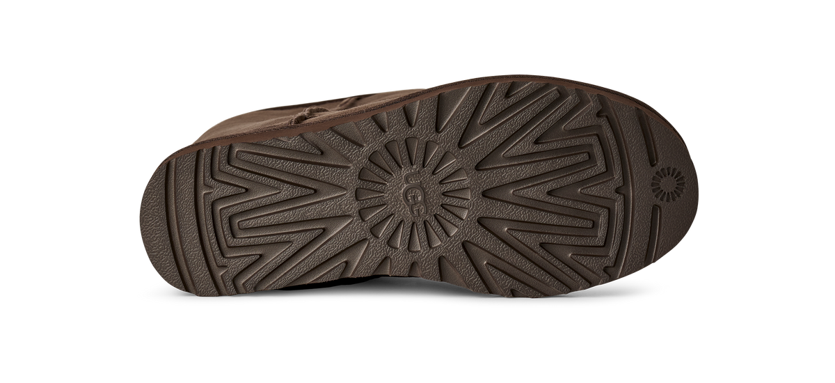 The textured brown rubber outsole of a shoe, showing a detailed tread pattern and a circular UGG logo embossed in the center, on a white background.