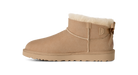 A single beige suede ankle boot with a cream shearling lining and a decorative bow on the back, shown in profile against a solid white background.