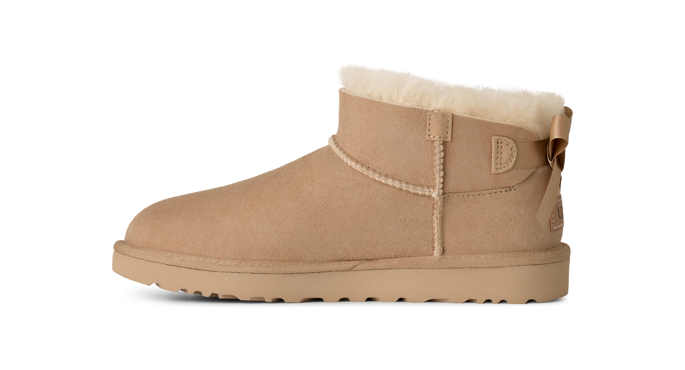 A single beige suede ankle boot with a cream shearling lining and a decorative bow on the back, shown in profile against a solid white background.