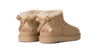 A pair of UGG Mini Bailey boots in tan suede with fluffy cream shearling lining and matching tan ribbon bows on the back, shown against a plain white background.