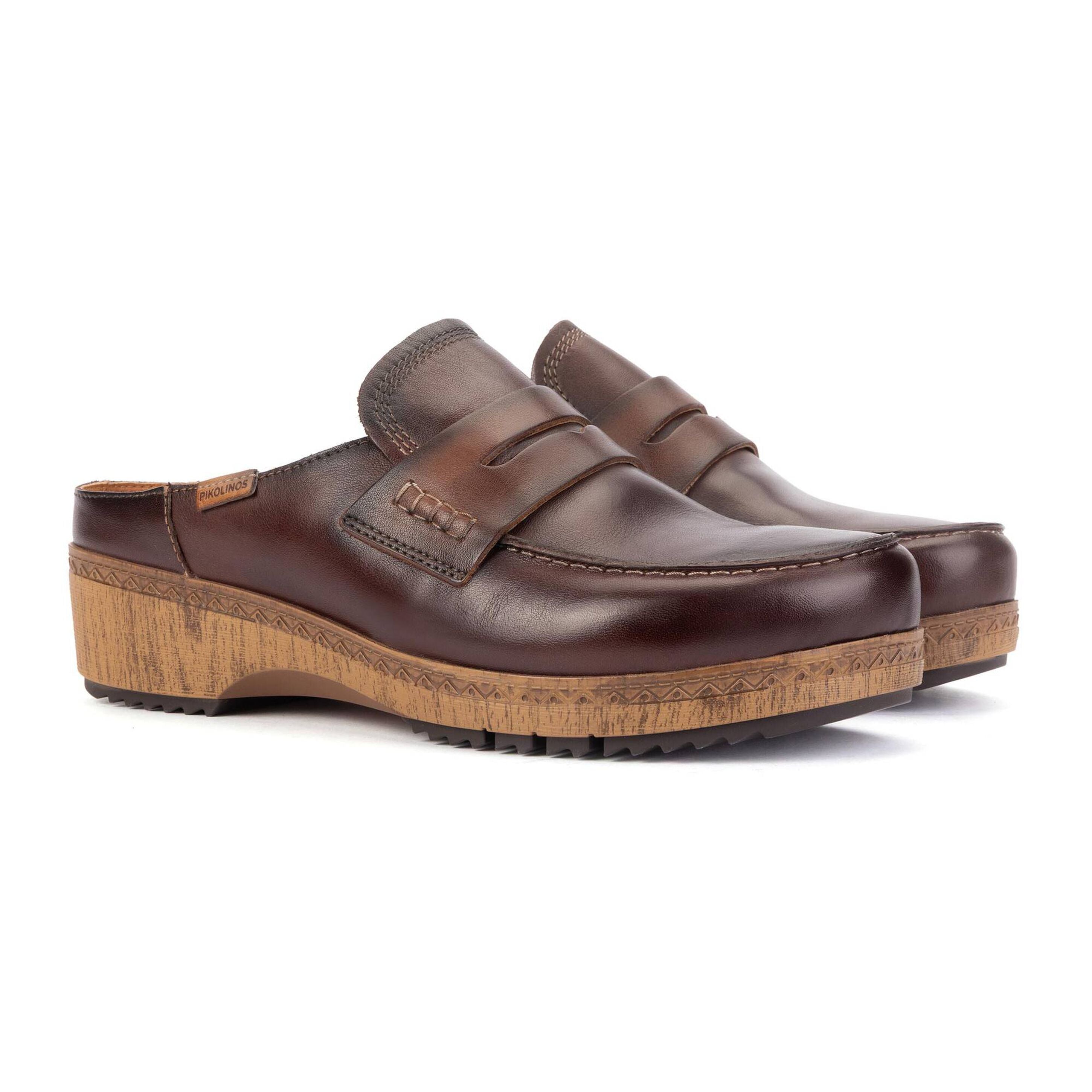 A pair of dark brown leather clog-style mule shoes with a cork-look wedge heel and sole, shown on a clean white background.