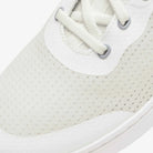 Close-up of a white sneaker with textured sole and laces on a light gray background