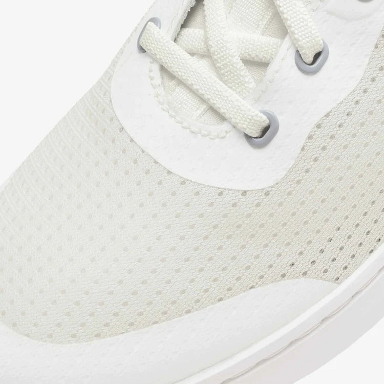 Close-up of a white sneaker with textured sole and laces on a light gray background