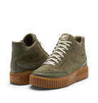 A pair of high-top sneakers by Sorel in olive green suede and leather, featuring chunky brown gum soles and off-white laces, set against a plain white background.