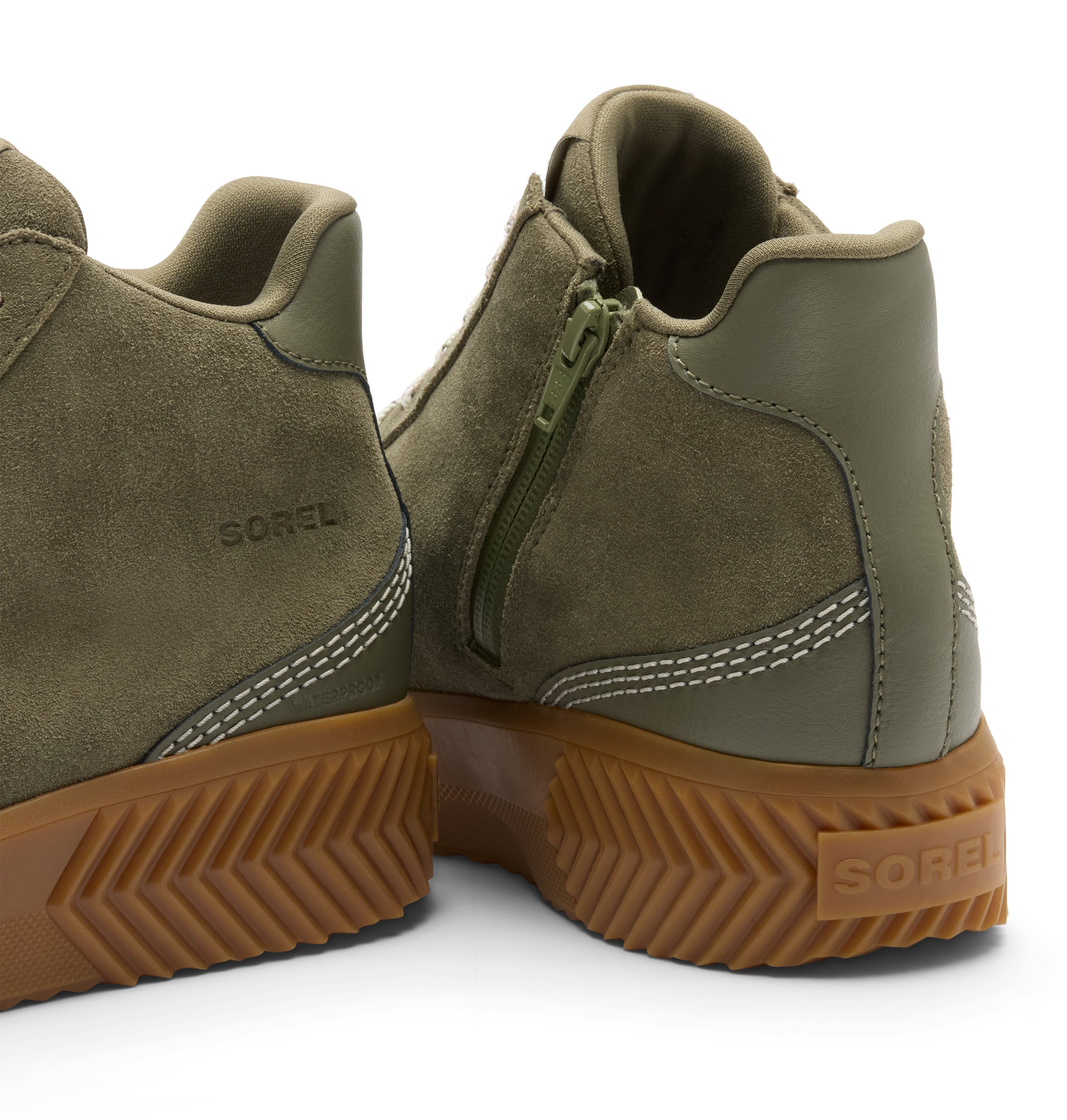 Close-up rear view of olive green suede and leather mid-top boots with side zippers and brown lug soles, shown on a white background. The SOREL brand name is visible on the heel and side.