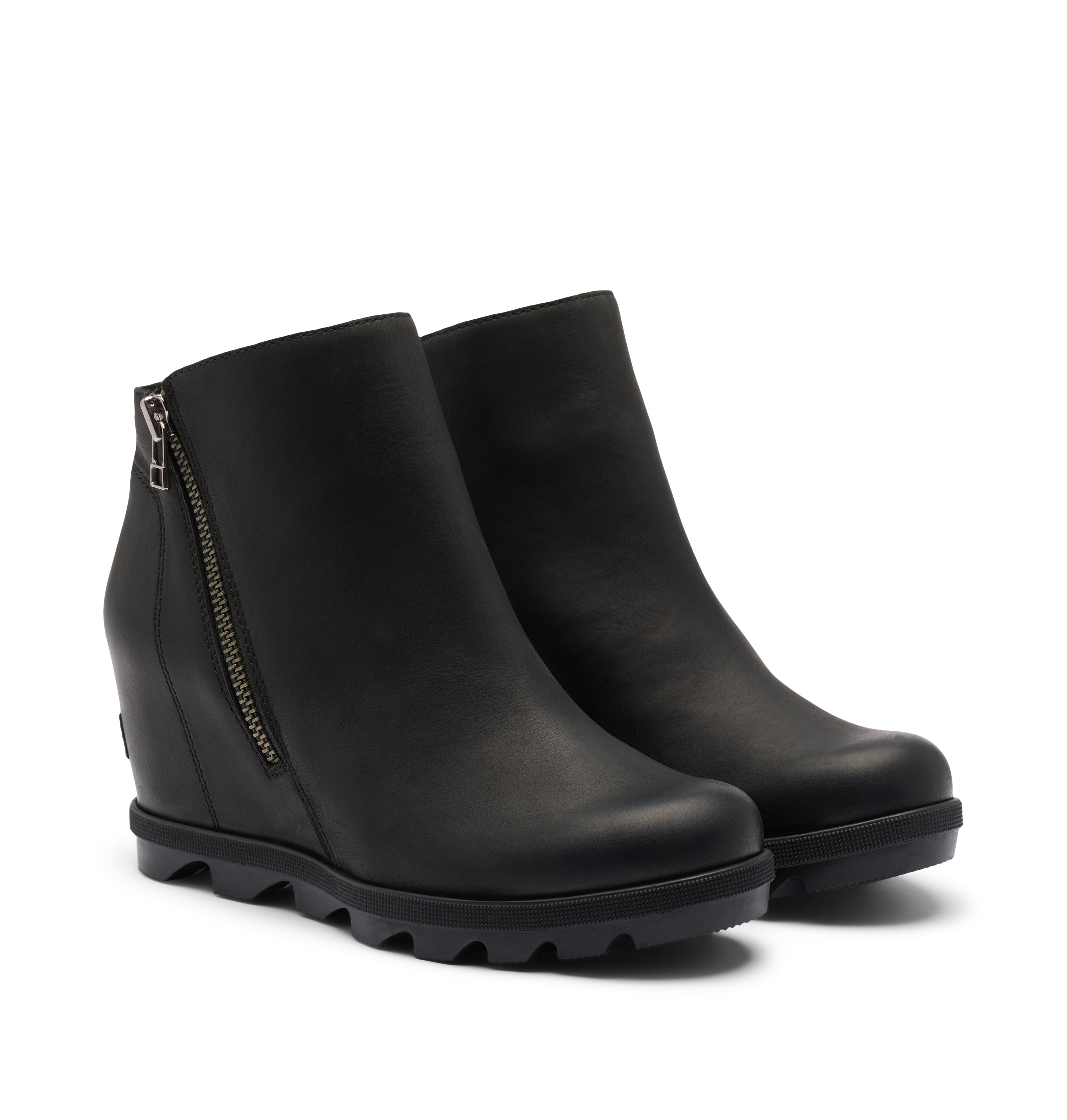 A pair of black leather wedge ankle boots with side zippers and chunky lug soles, shown on a light off-white background.