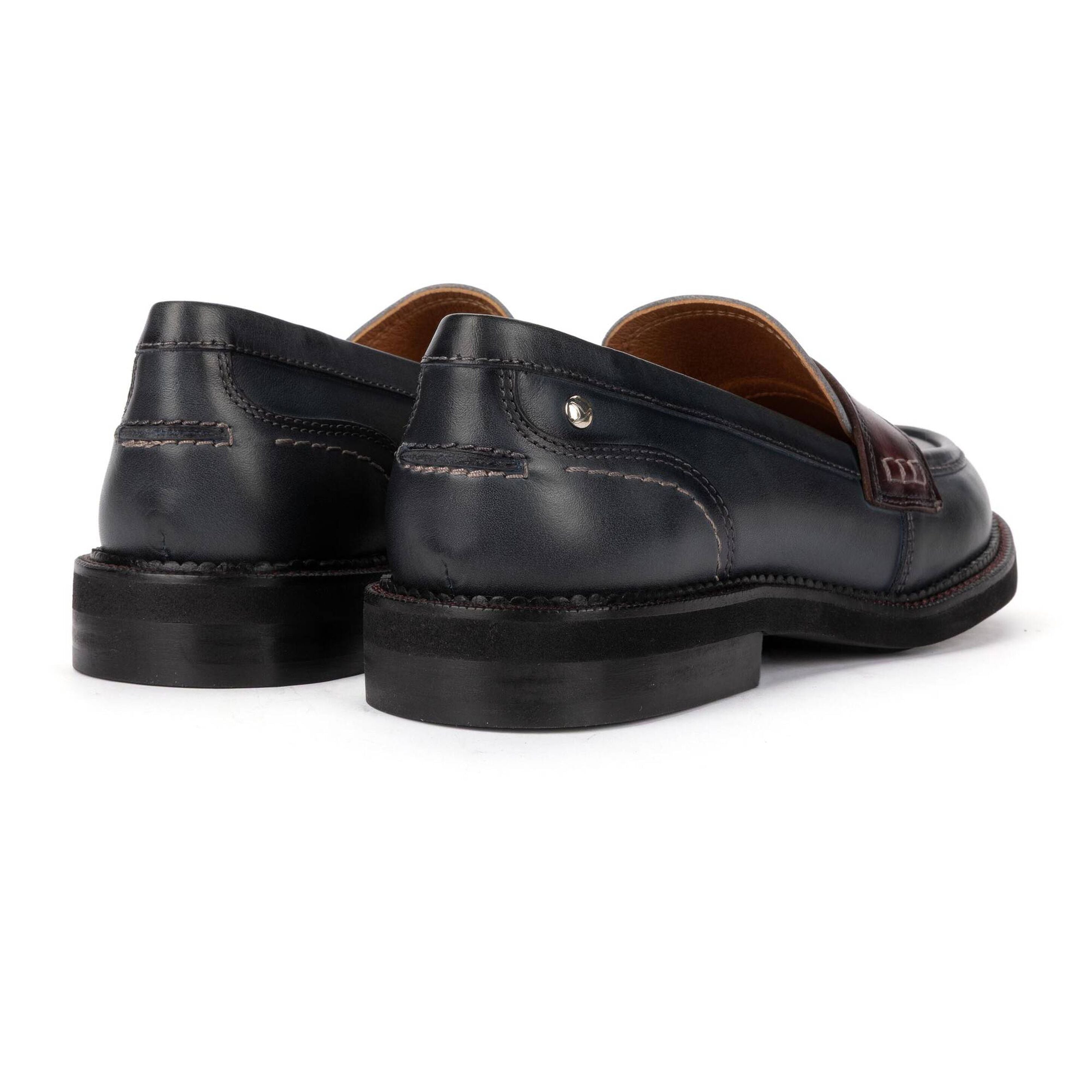 A pair of black leather penny loafers with brown lining and a brown leather brand tab on the side, shown from a three-quarters rear angle on a white background.
