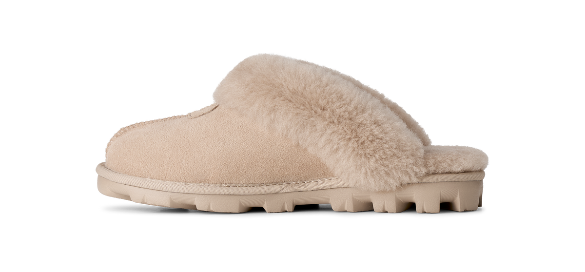 A single slip-on mule slipper in beige suede with a soft beige faux-fur collar and a chunky lug sole, shown in profile against a white background.