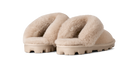 A pair of beige shearling-style slide slippers with thick, textured beige soles, shown from a three-quarters angle on a solid white background.