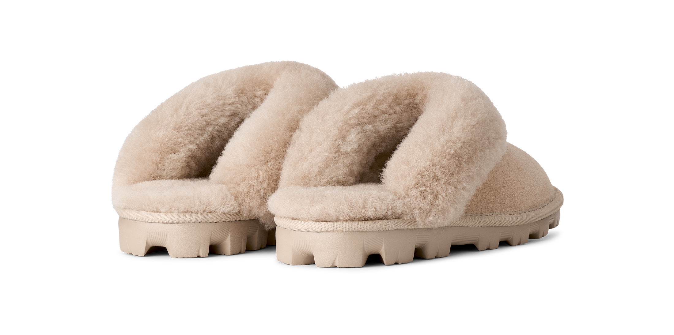 A pair of beige shearling-style slide slippers with thick, textured beige soles, shown from a three-quarters angle on a solid white background.