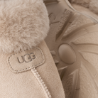 Close-up of a beige UGG boot showing the suede exterior, plush shearling lining, and embossed UGG logo patch.