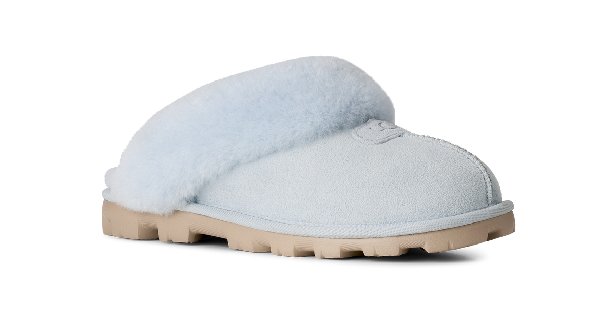 A single light blue slip-on slipper with fluffy pale blue shearling lining and a tan rubber sole, shown from a side profile on a white background.