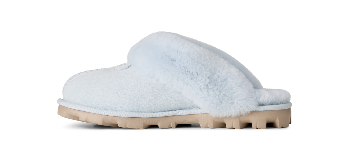 A light blue slip-on mule slipper with fluffy faux-fur trim and a chunky beige sole, shown in a side profile on a white background.