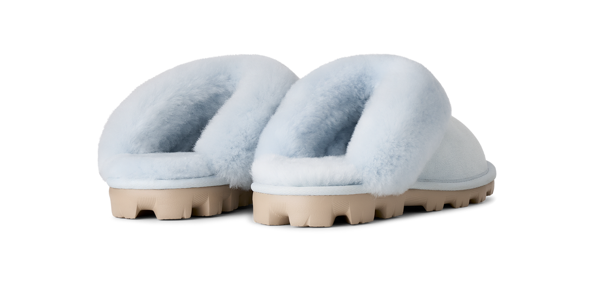 A pair of fluffy open-toe slippers with pale blue faux-fur uppers and chunky beige lug soles, shown from the back on a white background.