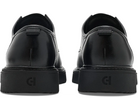 A pair of black leather lace-up shoes shown from the back, featuring thick black platform soles with a debossed monogram logo, photographed on a clean white background.