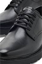 A close-up shot of a black leather lace-up shoe, showing the toe, laces, side panel, and part of the heel against a white background.