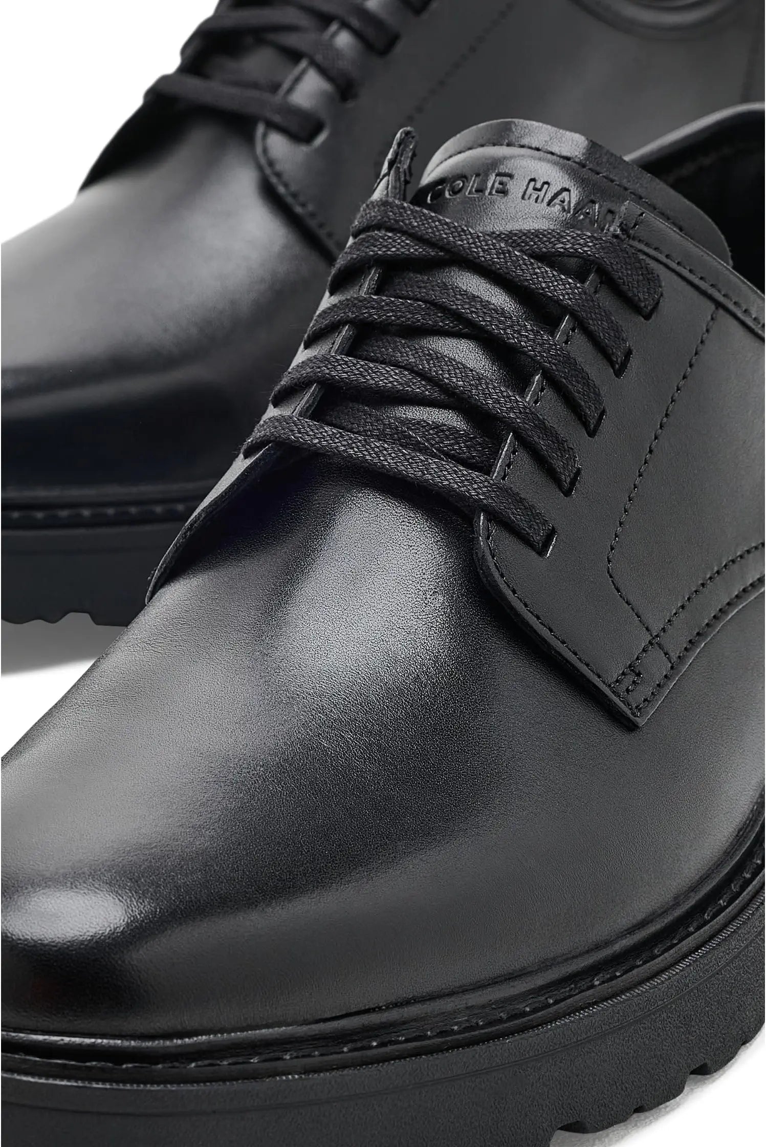 A close-up shot of a black leather lace-up shoe, showing the toe, laces, side panel, and part of the heel against a white background.