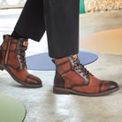 Brown leather boots worn with black pants on a light wooden floor.