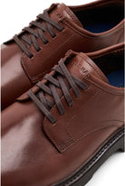 A close-up shot of a pair of brown leather lace-up dress shoes, showing the side and toe details against a clean white background.