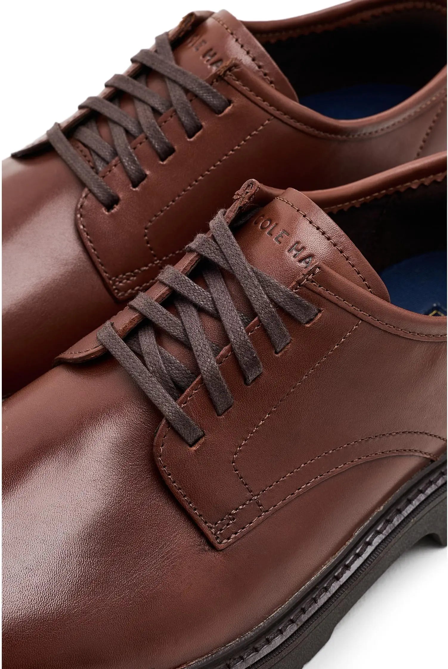 A close-up shot of a pair of brown leather lace-up dress shoes, showing the side and toe details against a clean white background.