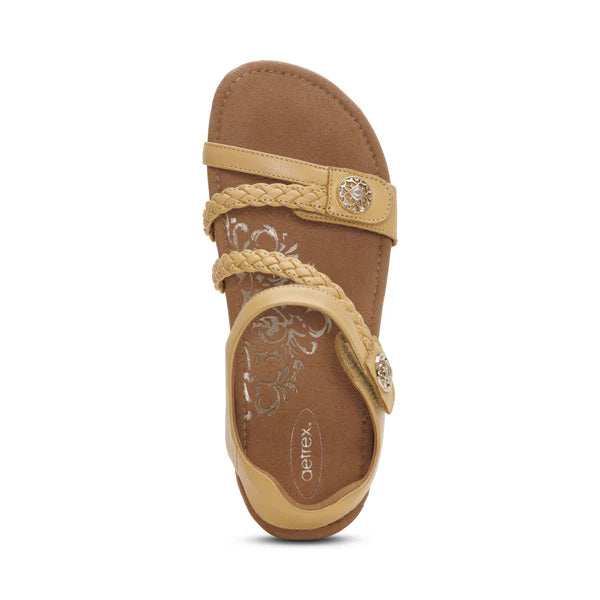 Tan sandal with braided strap and decorative buckle on a white background