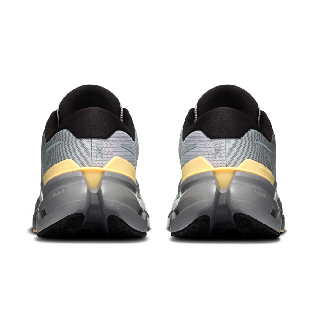 A pair of running shoes shown from the rear, featuring a light gray and black upper with a prominent yellow accent band and a thick dark gray and black sole.