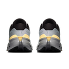 A pair of running shoes shown from the rear, featuring a light gray and black upper with a prominent yellow accent band and a thick dark gray and black sole.