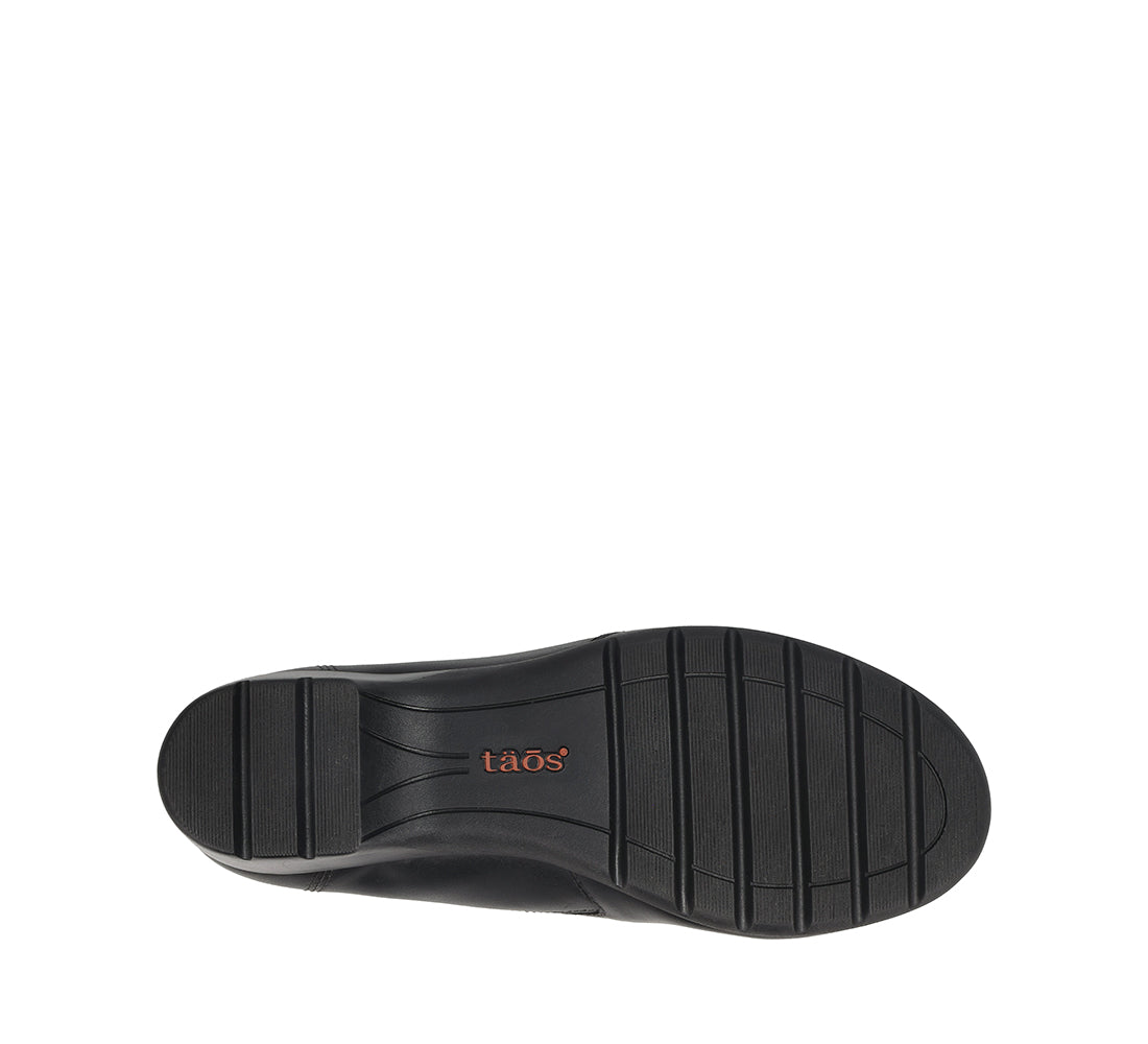 A top-down view of a black shoe sole with vertical tread grooves and the brand name 'taos' printed in orange on the heel, set against a plain white background.