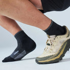 Beige and black athletic shoe with a person wearing black socks on a light gray background