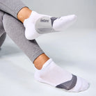 White ankle socks with gray accents worn by a person sitting on a light gray surface.