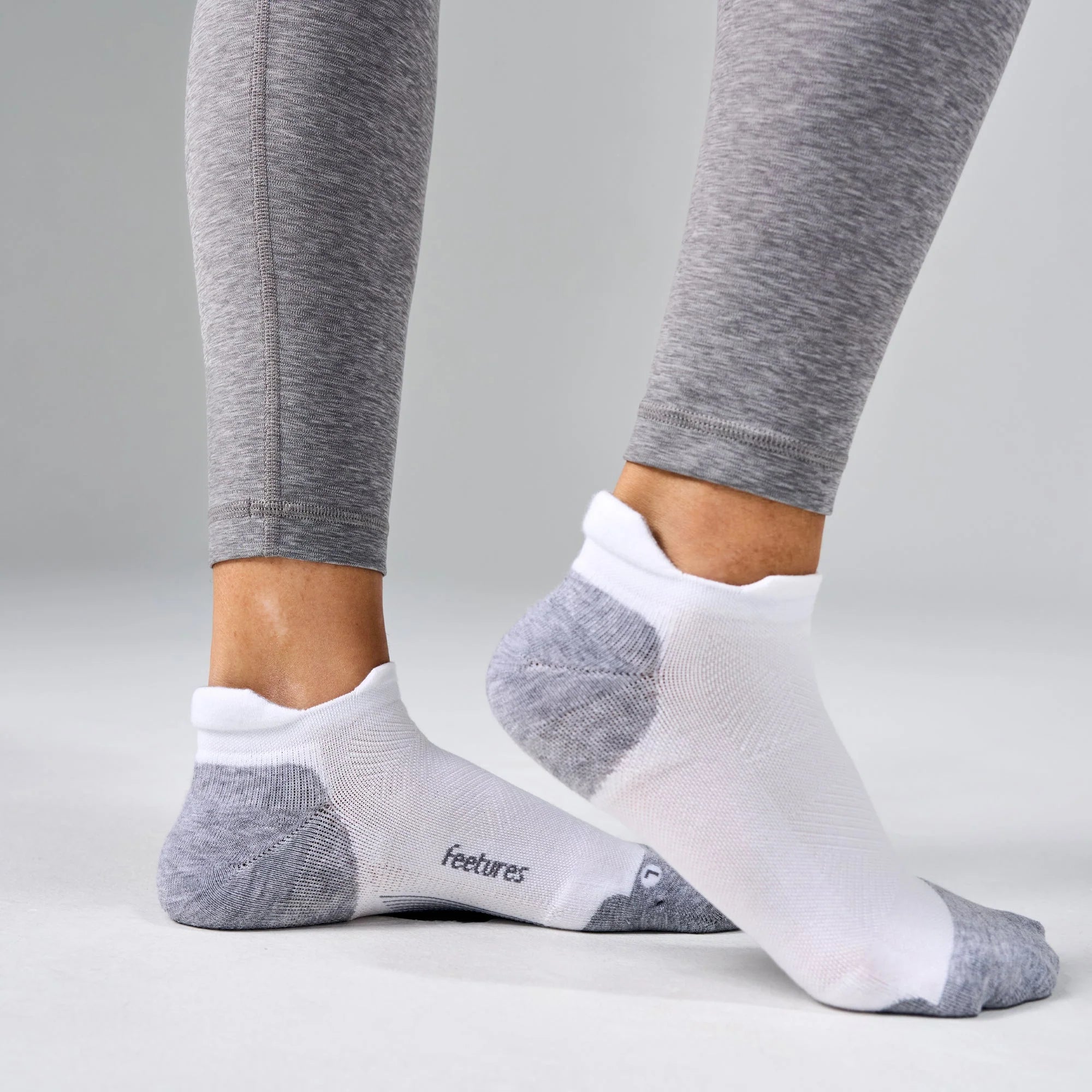 White ankle socks with gray accents worn with gray leggings on a light gray background
