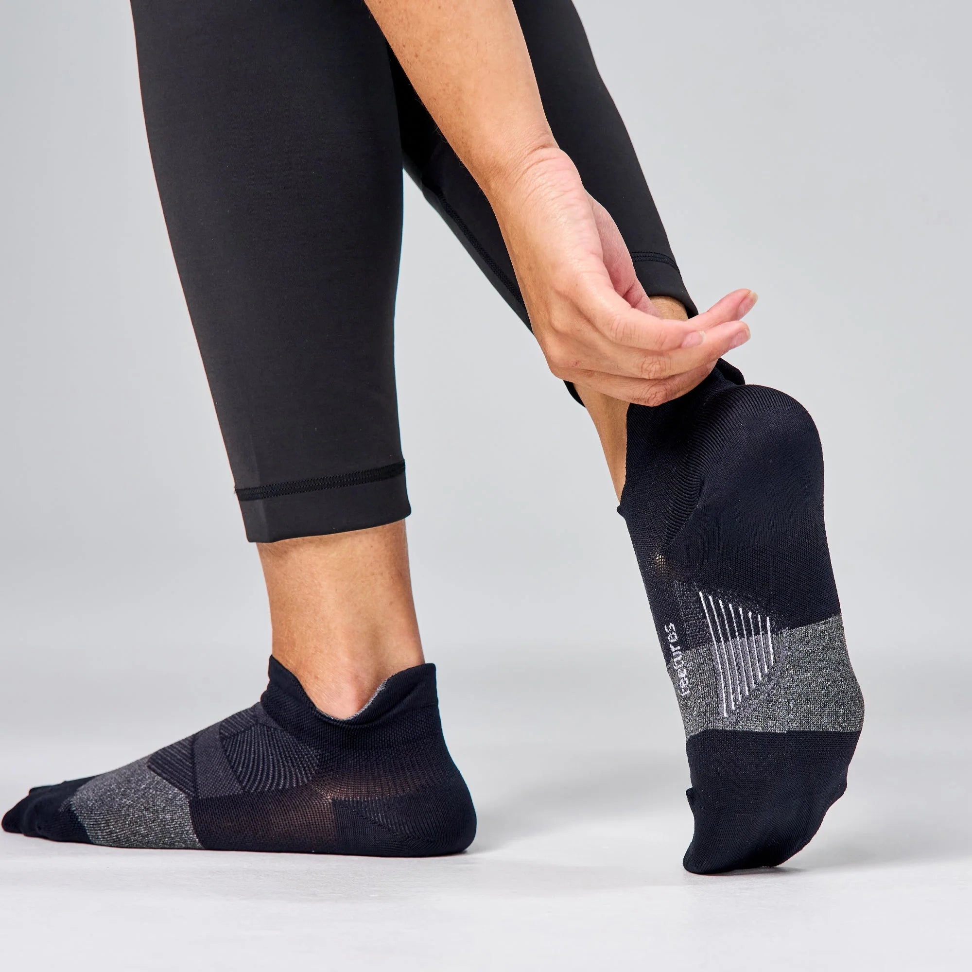 Person wearing black ankle socks with a gray sole on a light gray background