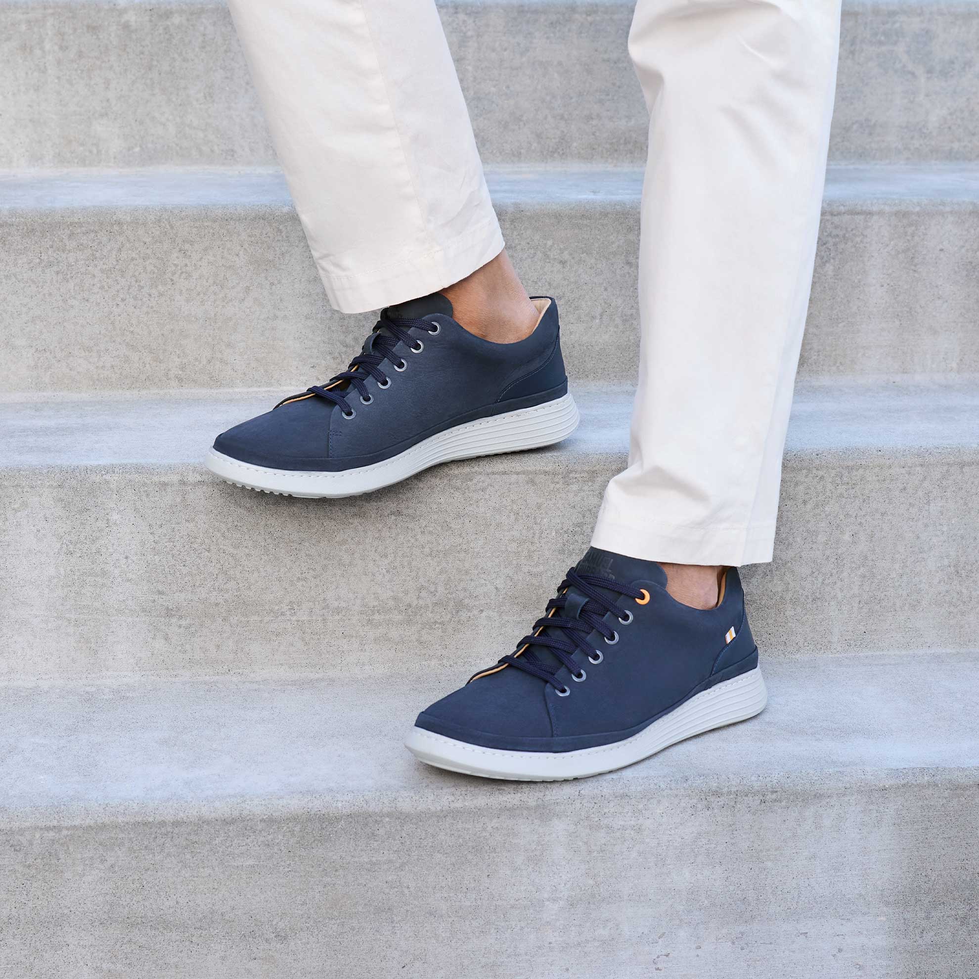 Navy blue sneakers with white soles worn by a person on concrete steps.