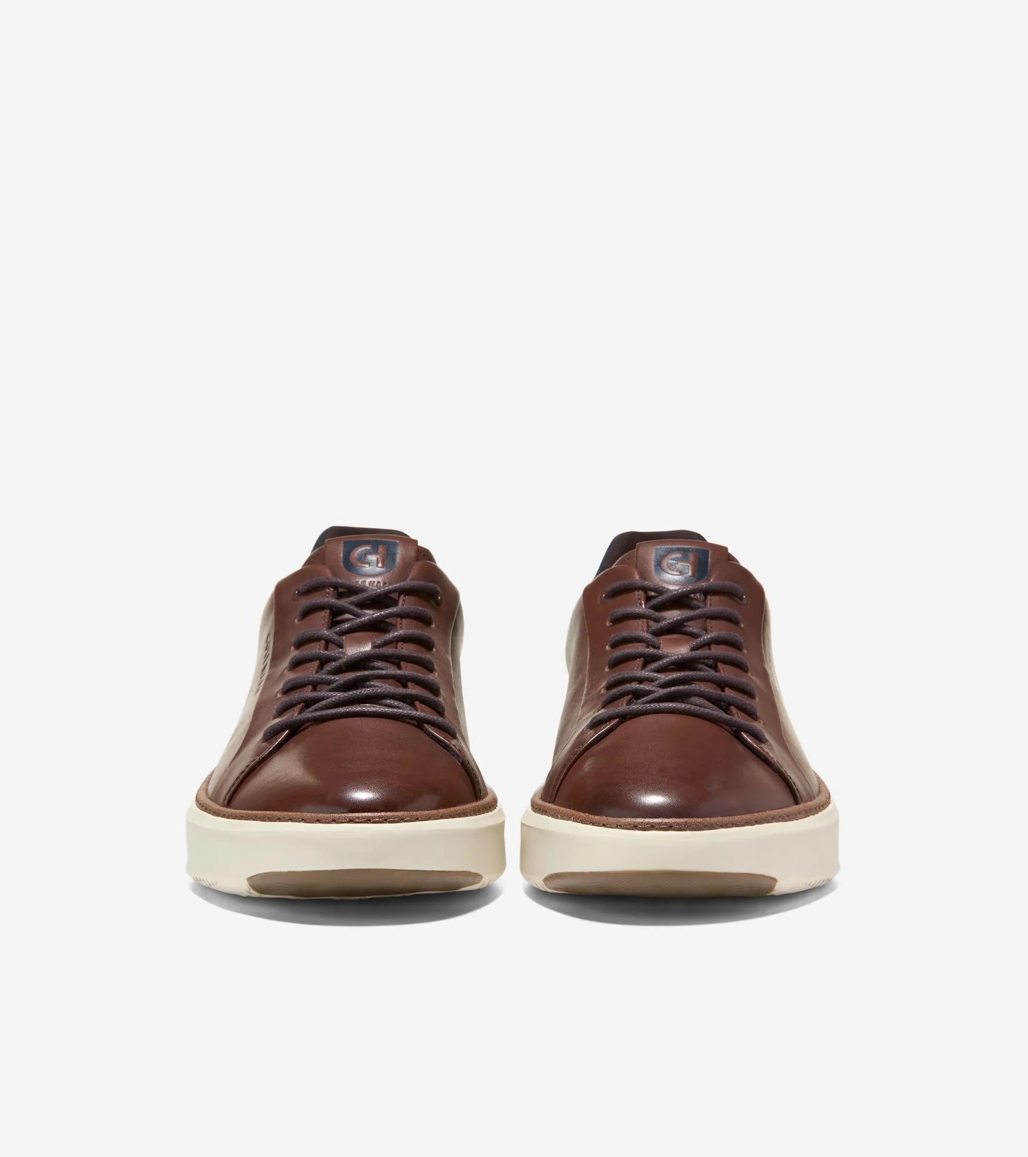 A pair of brown leather low-top sneakers shown from the front on a light gray background.
