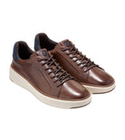 A pair of brown leather low-top sneakers with dark brown laces, cream-colored soles, and dark navy blue lining, displayed on a light gray background.