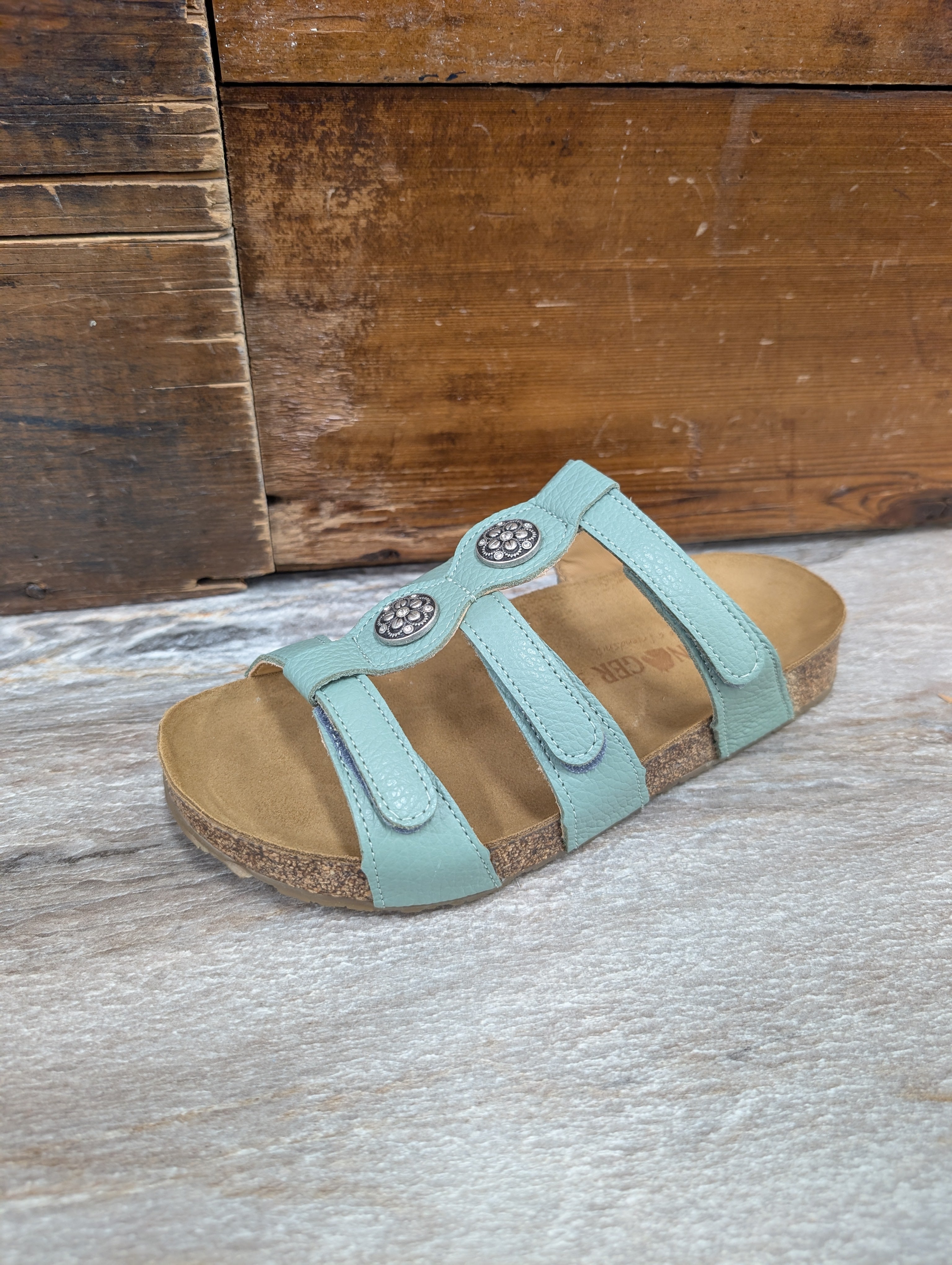 Teal sandal with brown sole on a wooden surface