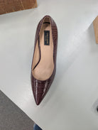 A single pointed-toe pump in a deep burgundy crocodile-embossed leather, shown from a top-down angle on a light gray surface. The insole is beige with a black brand label reading 'Cole Haan'.