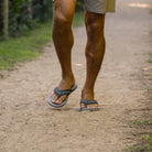 Person wearing sandals walking on a dirt path with grass and trees in the background
