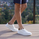 Person wearing white sneakers with brown accents on a wooden deck.