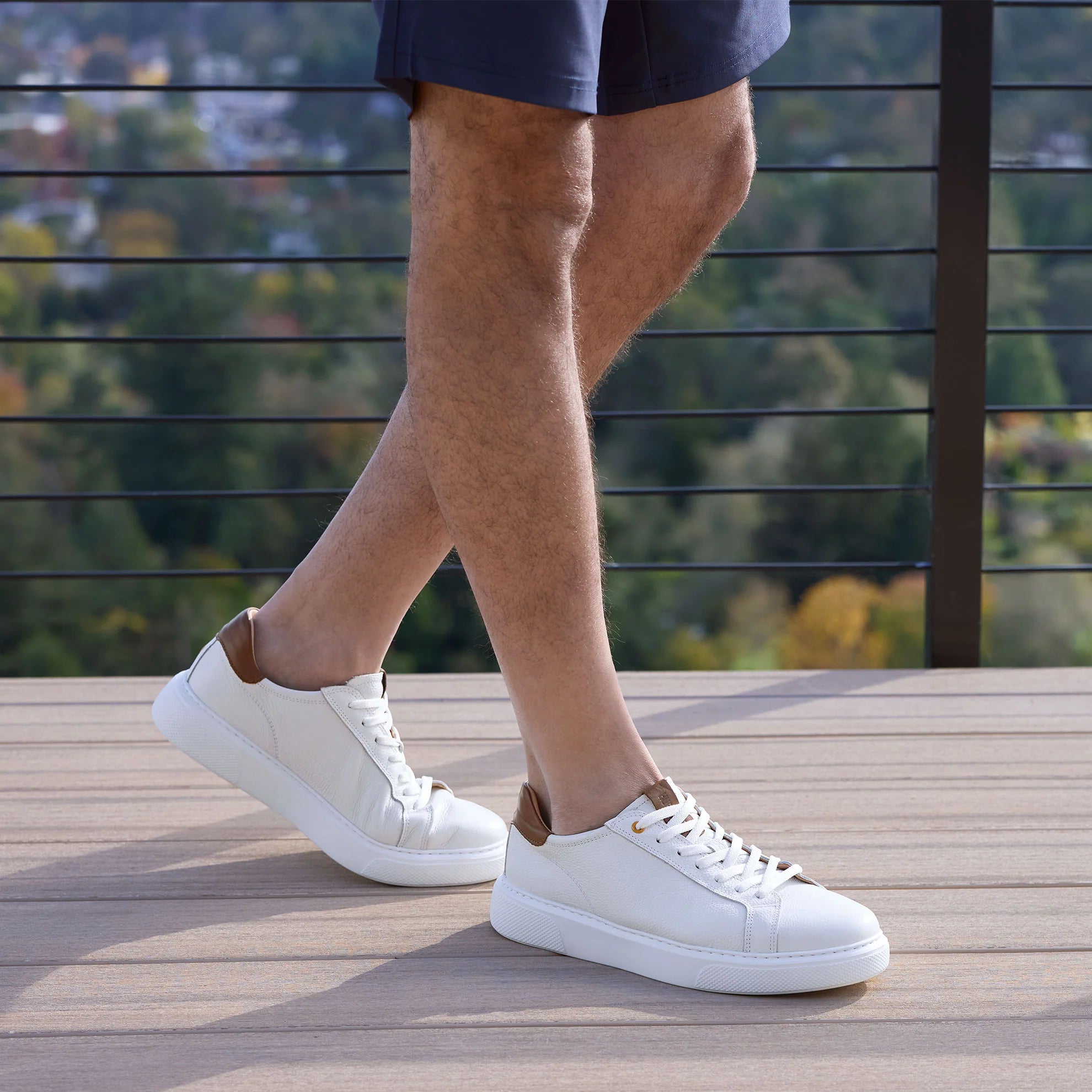 Person wearing white sneakers with brown accents on a wooden deck.