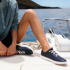 Person wearing navy blue sneakers with white laces on a boat by the water.